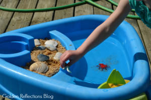 Playing with beach themed water sensory table for toddlers.