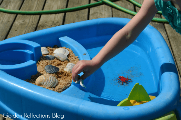 Playing with beach themed water sensory table for toddlers.