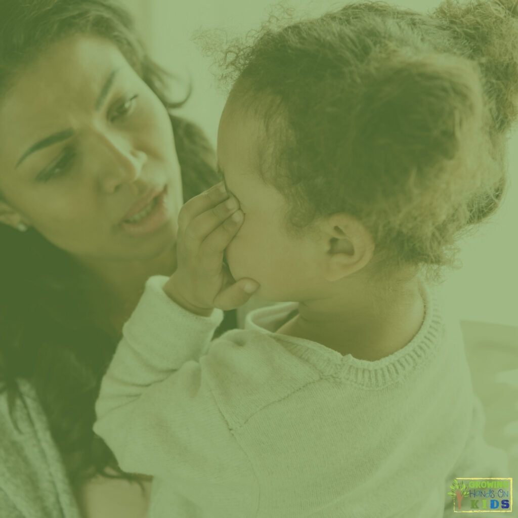 mother holding upset little girl who has her hands over her eyes. 