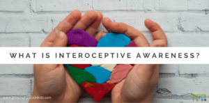 white brick background with child's hands hold a multi-colored clay heart. White text overlay with gray words that say "What is interoceptive awareness?"