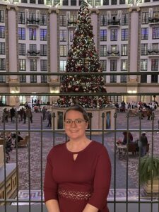 Inside a hotel decorated for Christmas. Young woman in a red dress sitting in front of a large Christmas tree.