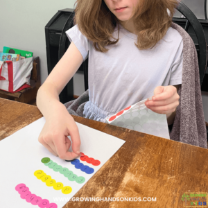 Picture of a young girl placing dot stickers on a piece of white paper to spell out spelling words.