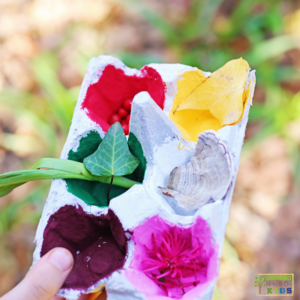 Child holding a painted egg carton with matching nature objects inside during a nature color hunt fine motor activity.