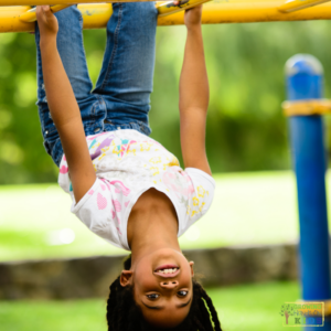 A young girl handing upside down on a set of monkey bars on the playground.