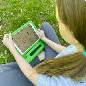 Child sitting on grass outdoors using a tablet in a green case to read a digital book on the Reading Eggs app. The screen shows an illustrated storybook with text and images.