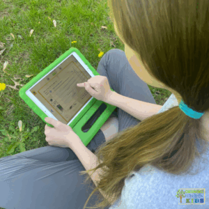 Child using a tablet in a green case while sitting on grass, interacting with a digital book in the Reading Eggs app. The screen shows a reading activity or comprehension quiz.