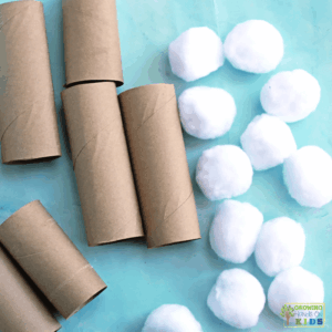 Cardboard paper rolls cut to different heights and white pom poms arranged on a blue surface, set up for a snowball balancing fine motor activity for kids.