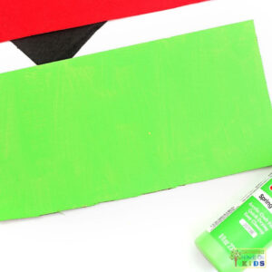 Cardboard painted bright green for the base of a ladybug fine motor activity, with a bottle of green paint nearby.