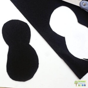 Black felt cut into a simple ladybug body shape with scissors and remaining felt nearby for a fine motor craft activity.