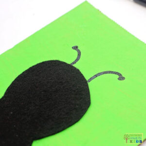 Black felt ladybug body glued onto green painted cardboard with drawn antennae for a fine motor buttoning activity.