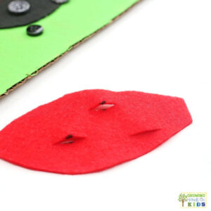Red felt ladybug wing with small slits cut for threading over buttons in a fine motor activity.