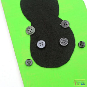 Black buttons glued onto a black felt ladybug body on green cardboard, creating spots for a buttoning fine motor activity.